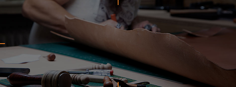 Craftsperson cutting and shaping leather for a custom holster on a workbench with leatherworking tools.