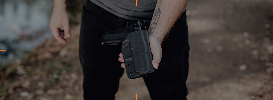 Man holding a black Kydex holster with a handgun outdoors.