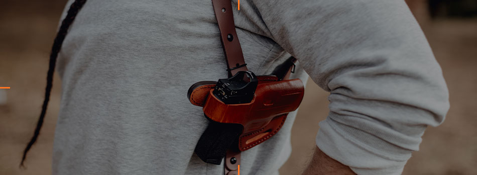 Man carrying a handgun with a red dot sight in a brown leather shoulder holster.