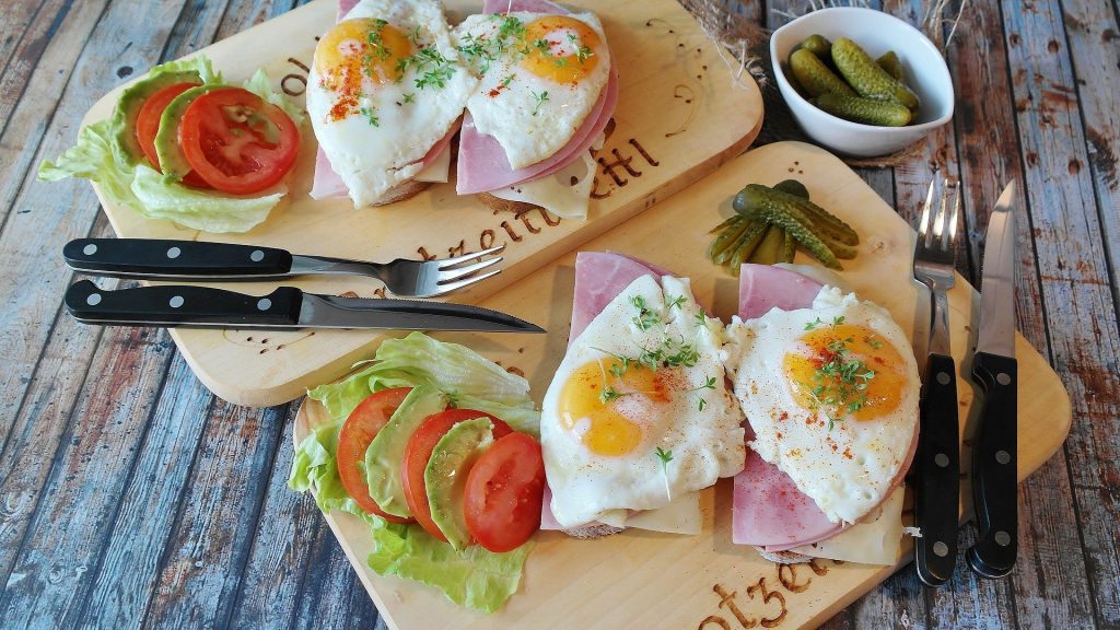 Foto de alimentos: tomates e lechuga cortados, huevos, jamon y queso. Al costado, los cubiertos: cuchillos y tenedores.  Aprovechar los alimentos.