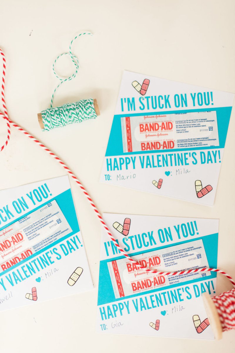 Three Valentine’s Day cards feature a band-aid and the message “I’m Stuck on You! Happy Valentine’s Day.” Two spools of colorful craft thread are placed around and over the cards.
