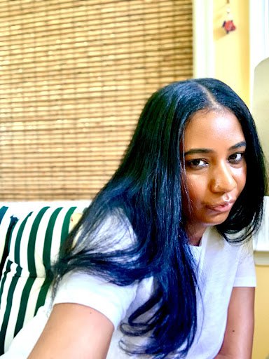 Morgan is sitting on a green-and-white-striped chair, wearing a white shirt, and looking at the camera.