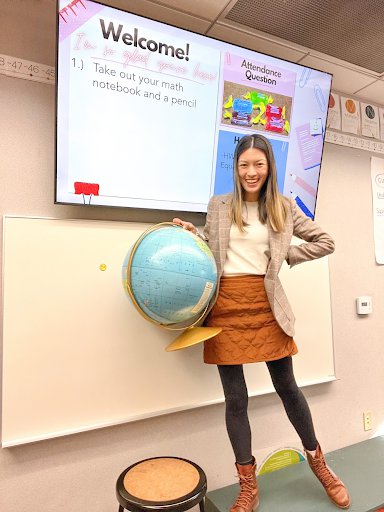Stephanie holds a globe and stands in front of a screen. Projected on the screen, it says, “Welcome! I’m so glad you’re here.”