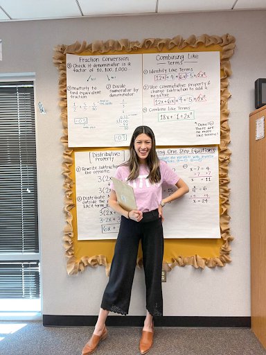 Stephanie stands in front of four large charts covered in handwritten math lessons. She sports a pink t-shirt reading”π π π.”