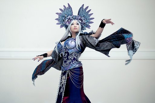 Yaya poses in an original fantasy costume she designed called the Empyrean Empress. She wears an ornate fantasy gown with flowing brocade sleeves, swirling appliqués and metallic armor accents in shad