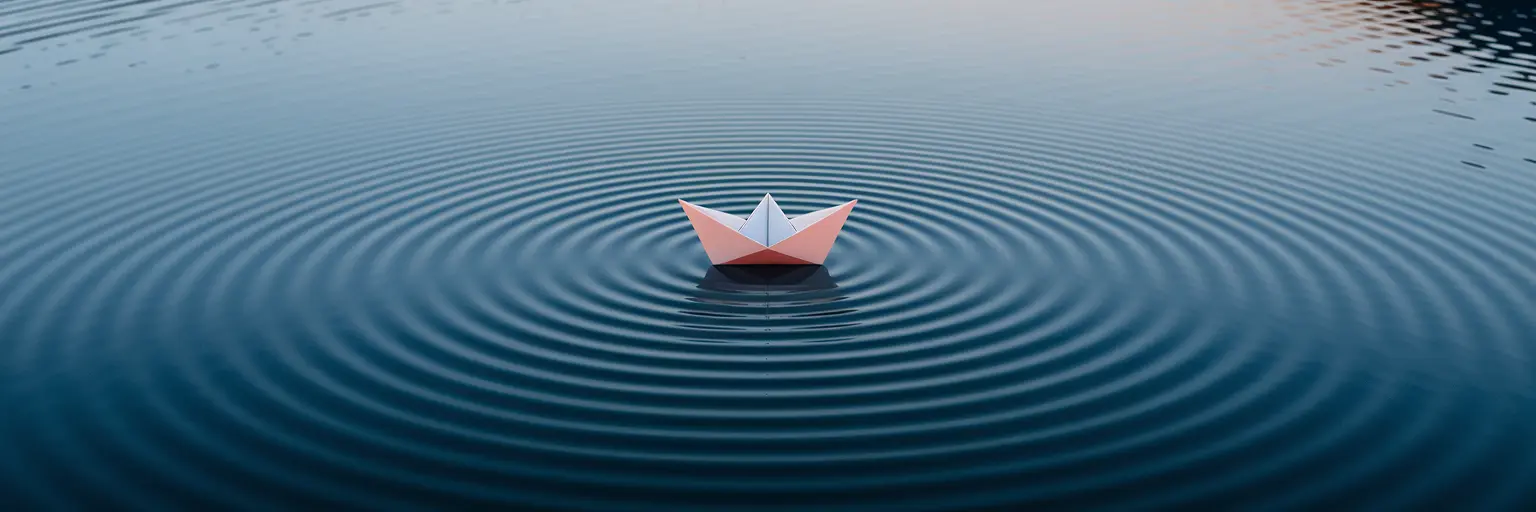 Paper boat creating wide ripples in water.