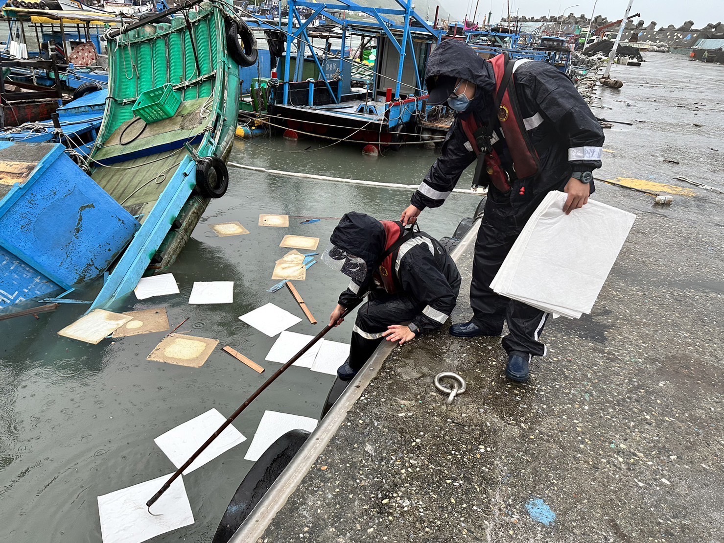 安檢所人員冒雨在車輛落海週邊布放吸油棉片處理溢漏油汙。（圖／第一二岸巡隊提供）