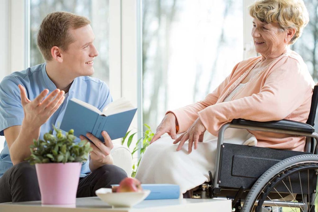 A senior woman sitting in a wheelchair visits with her son.