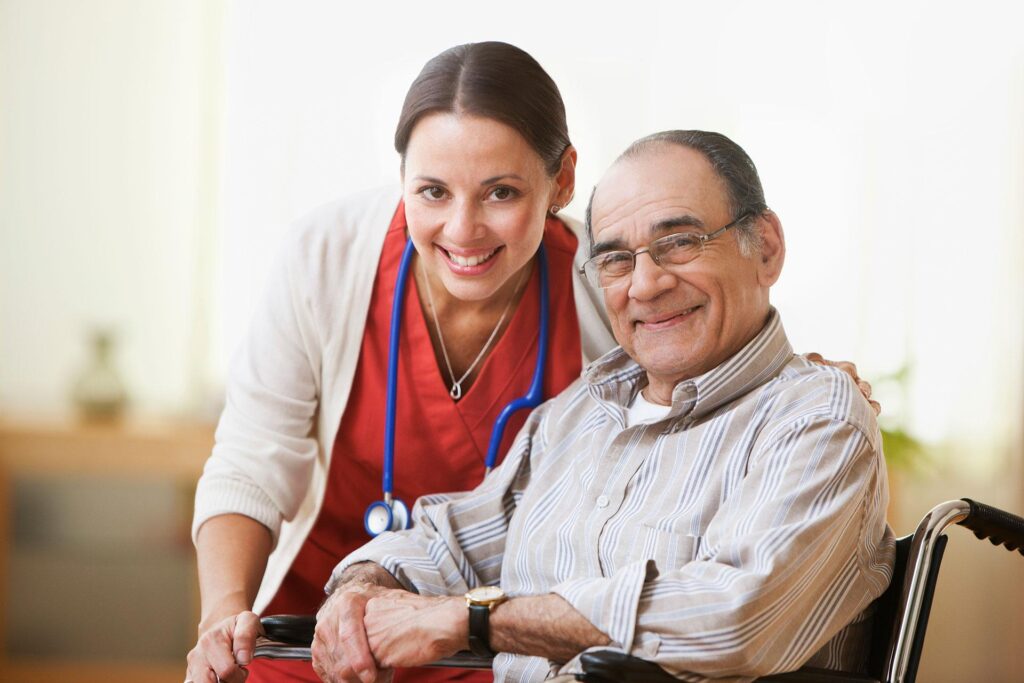 A nurse and resident sitting in a wheelchair smile for a picture.