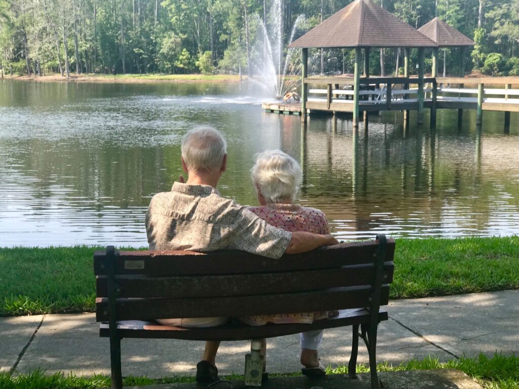 A senior couple sit on a bench, looking out over the lake by Cypress Village.