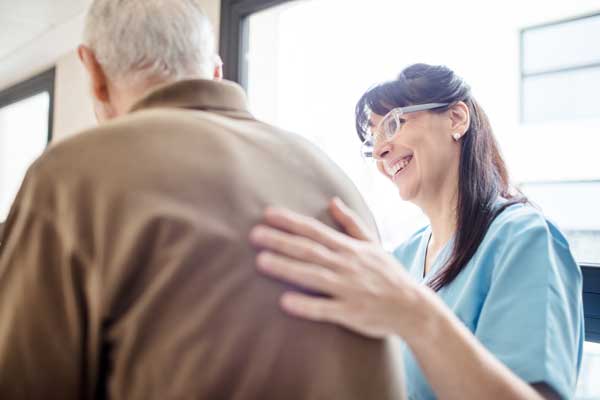 A smiling staff member pats a senior man on the back.