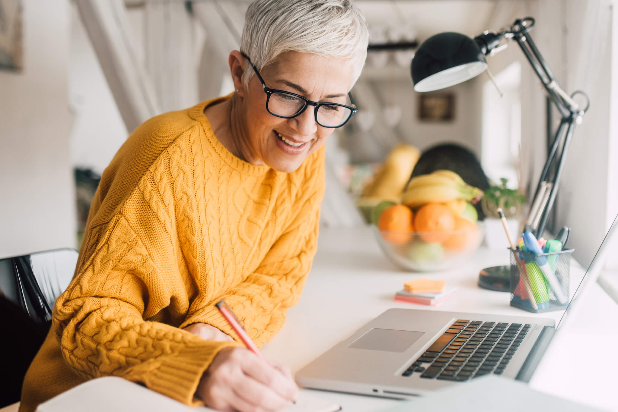 A senior woman works at a desk station on a laptop.