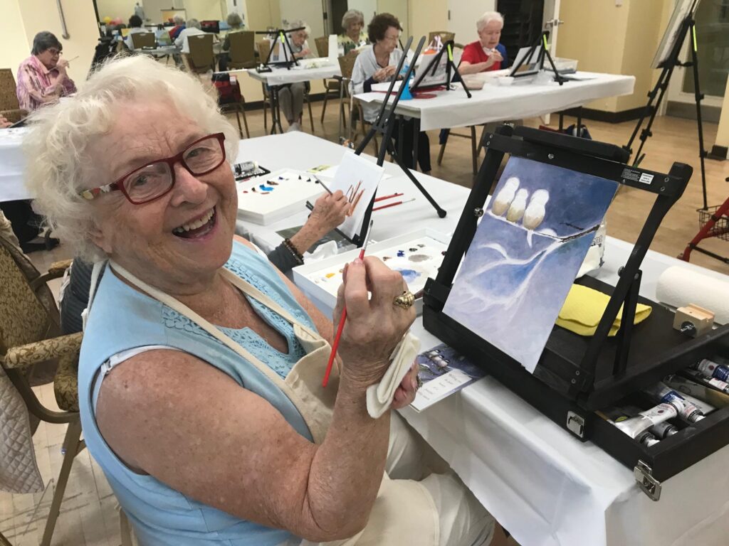 a senior woman paints on canvas in a painting class