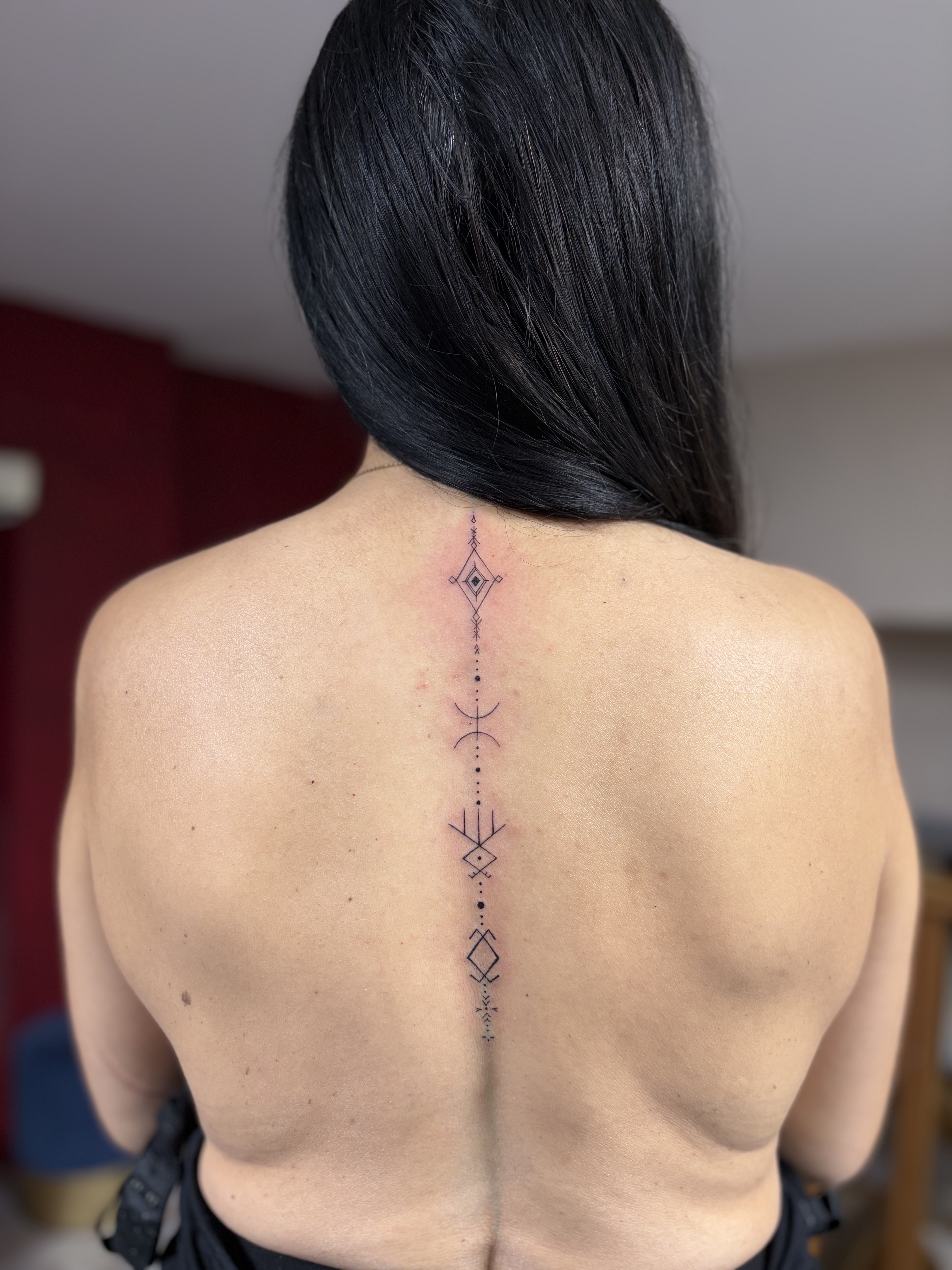 Ce tatouage présente un design géométrique élégant et minimaliste s'étendant verticalement le long de la colonne vertébrale…