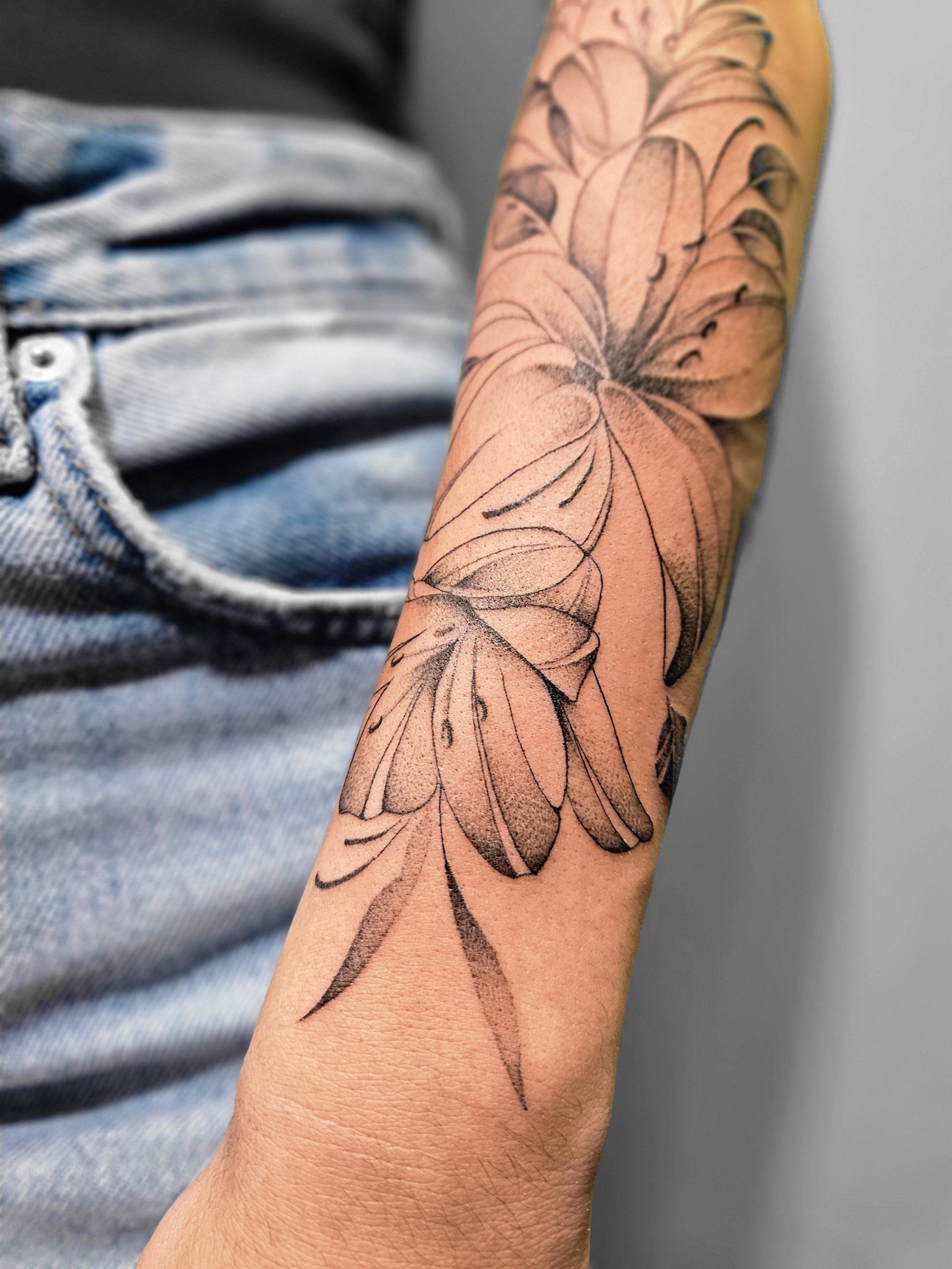 Ce tatouage présente un design floral élégant réalisé dans un style fine-line sur l'avant-bras. Il met en scène plusieurs…