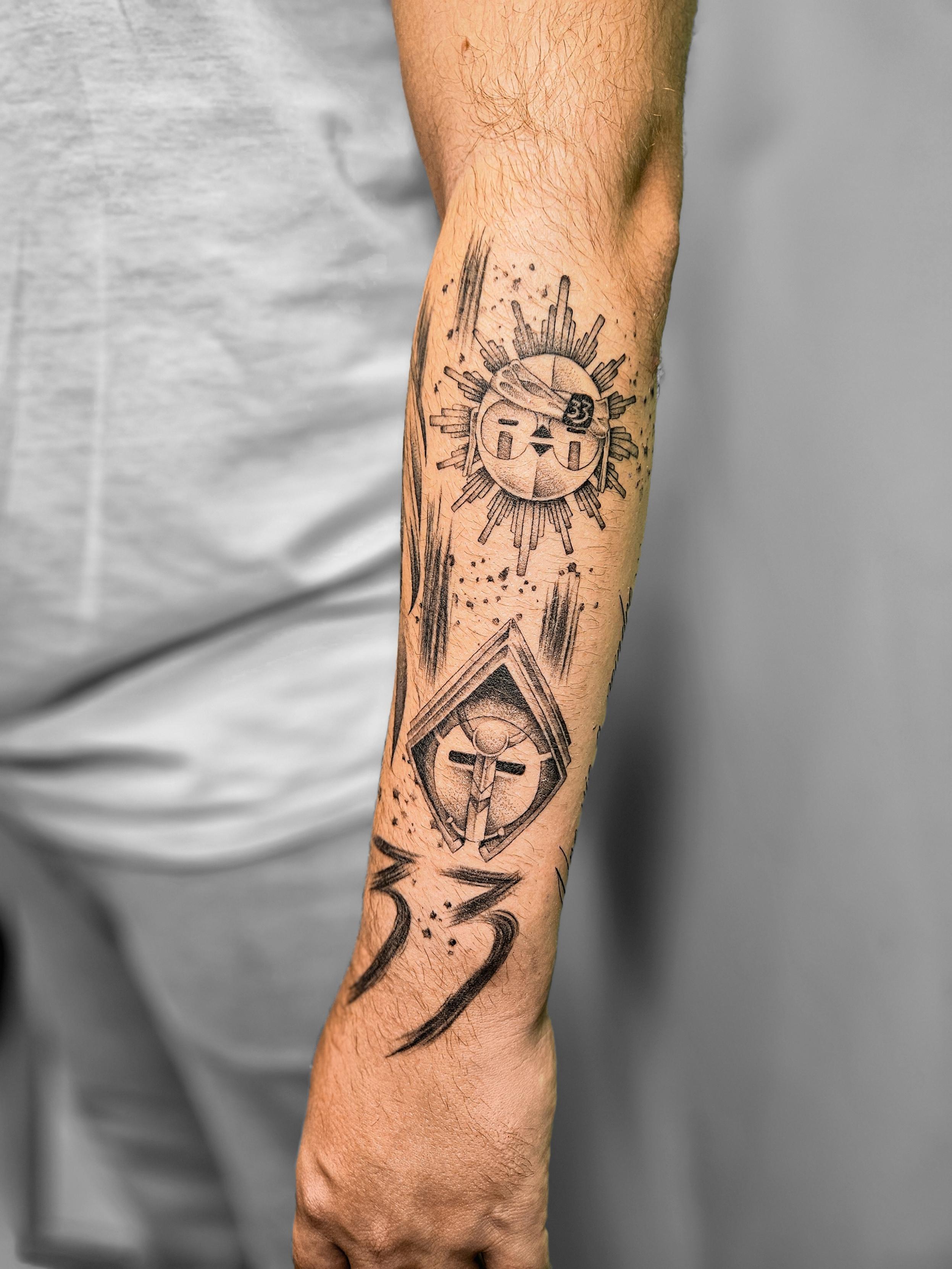 Ce tatouage à l'encre noire se compose de trois éléments principaux disposés verticalement sur l'avant-bras. En haut, un…