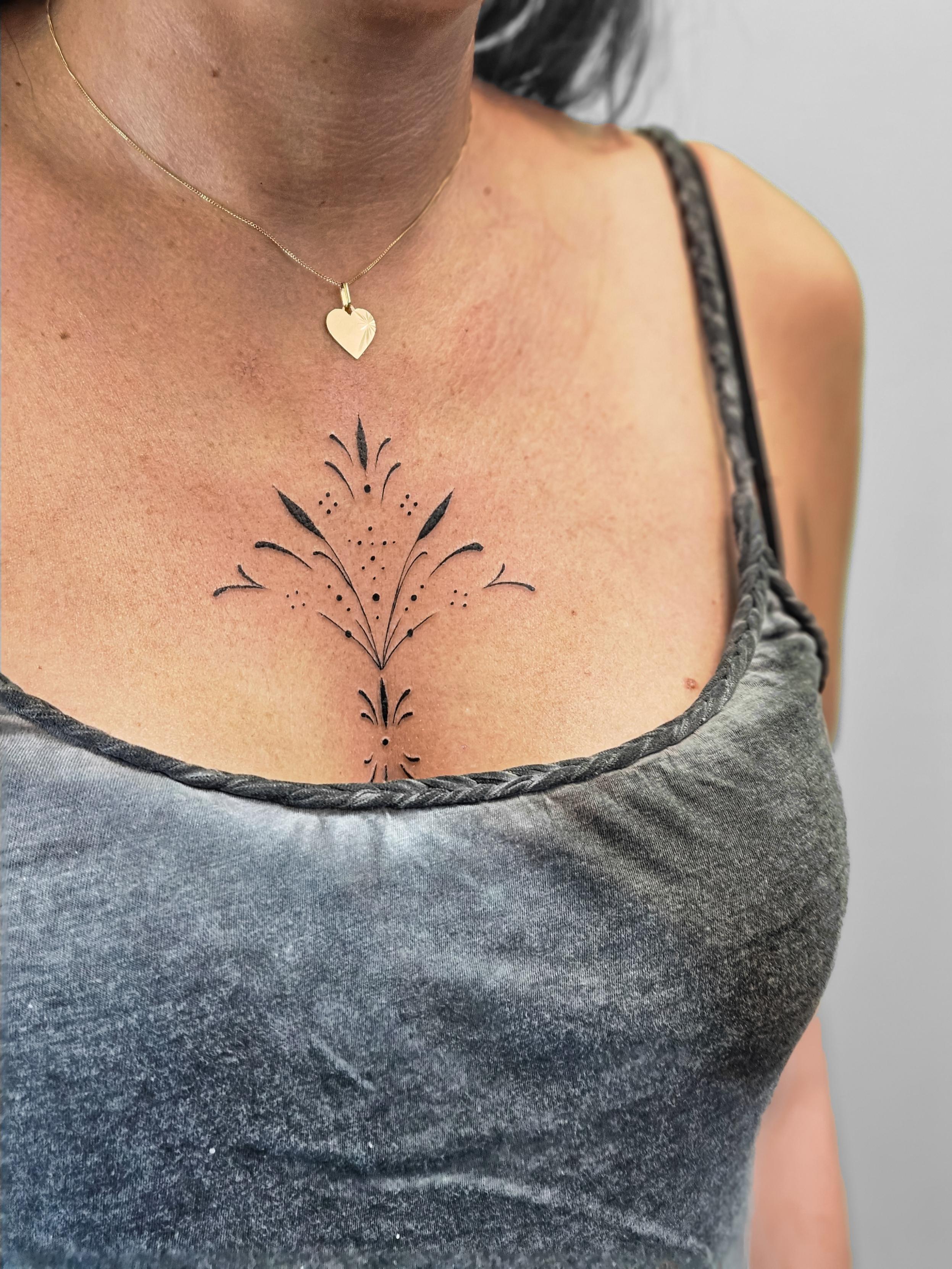 Ce tatouage délicat est situé sur le décolleté, au centre de la poitrine. Il représente un motif floral ornemental stylisé…
