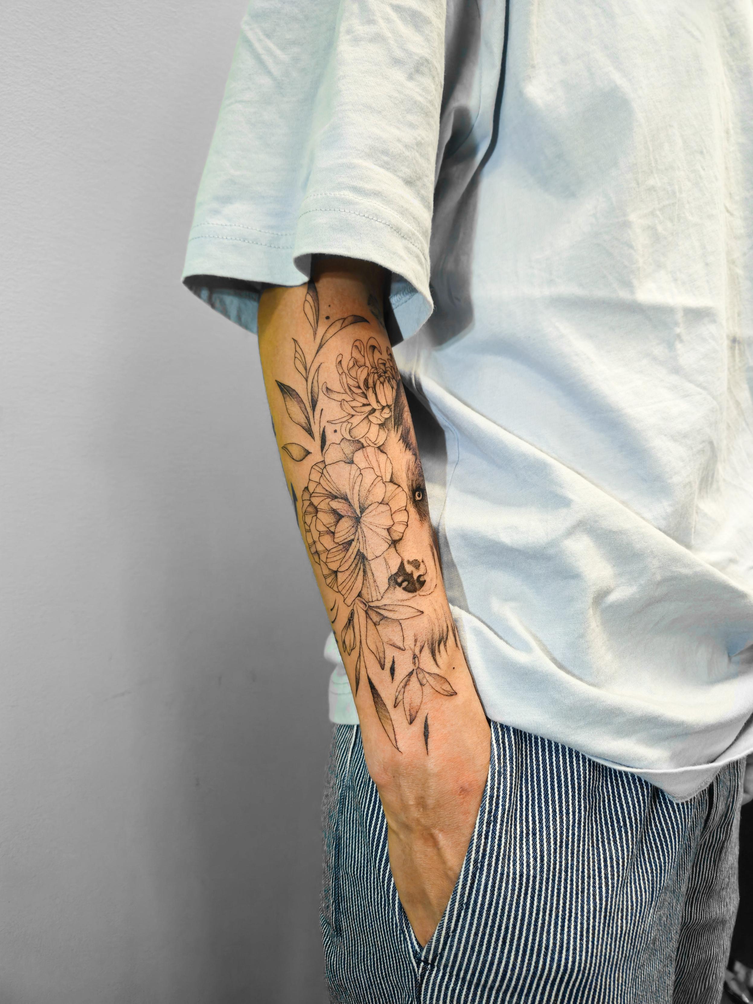 Ce tatouage floral en fine-line orne l'avant-bras dans sa longueur. Il présente une composition élégante de fleurs…