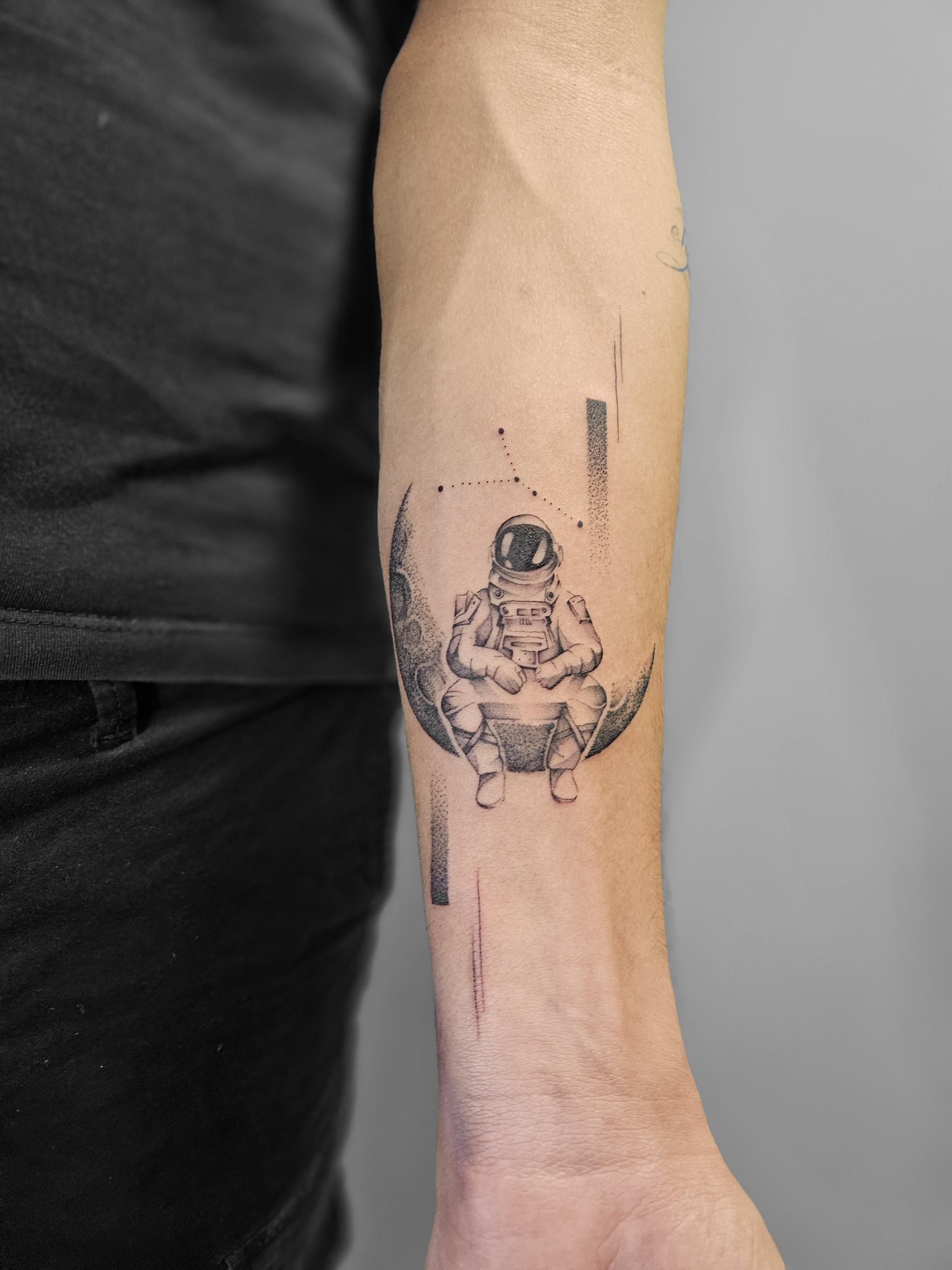 Ce tatouage représente un astronaute assis en position de méditation ou de contemplation sur un croissant de lune. L'œuvre…