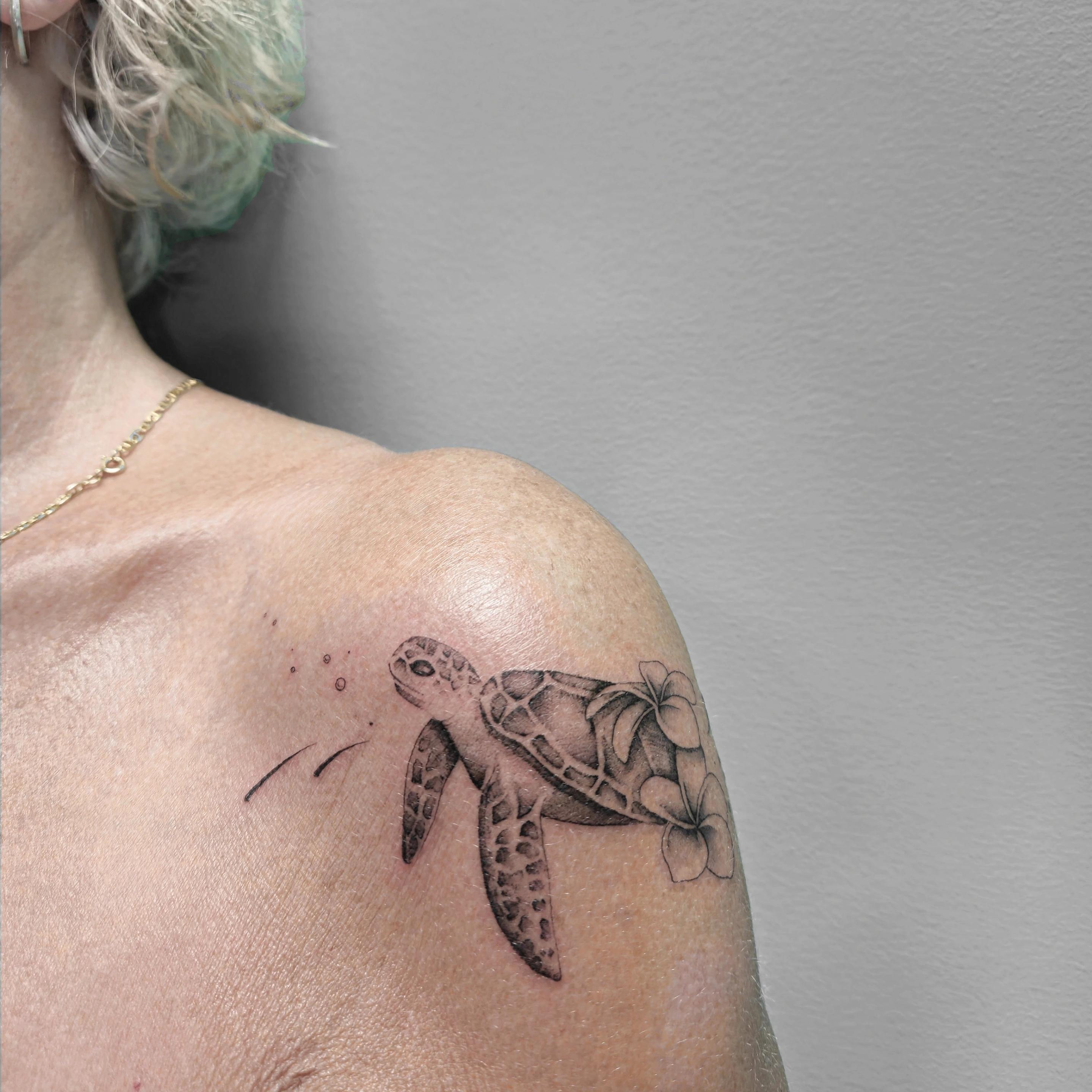 Ce tatouage représente une tortue de mer réalisée dans un style fine-line avec des détails délicats. La tortue est tatouée…