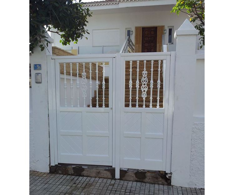 Puerta de aluminio blanca, con un fijo lateral una puerta abatible. Compuesta por travesaños, lama de machimbrado y en la parte alta balaustres