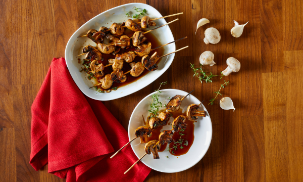 Mushroom skewers served on a white plate with a side of garlic and thyme. Red cloth napkin placed to the left of the plate.