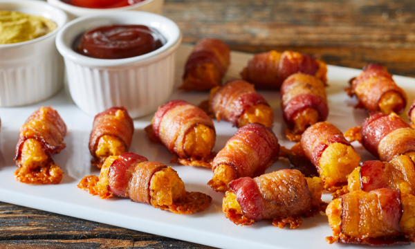 Potato Tots wrapped in bacon and served on a plate with dipping sauces. 