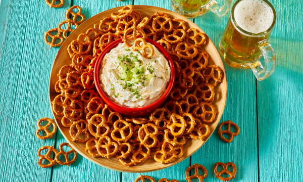 Pretzels on plate with beer cheese dip in the middle. Served with a glass of beer. 