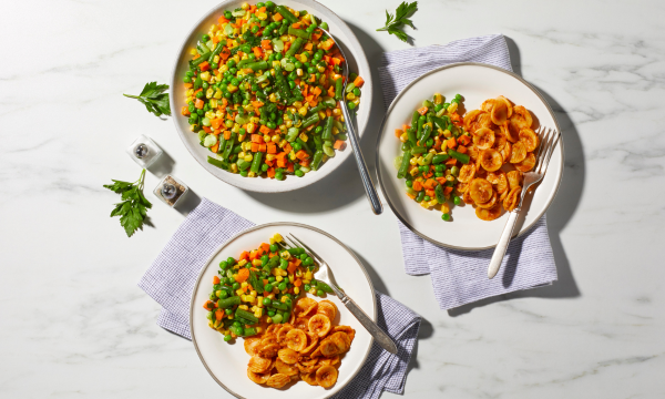 Carrots, peas, and corn on a white plate with pasta. 