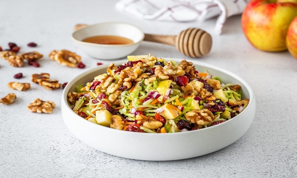 Bowl of salad topped with walnuts and cranberries, and a side of honey. 