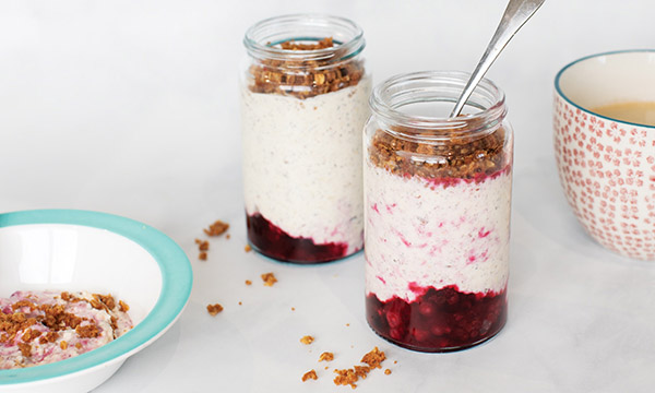 Two layered jars of yogurt with granola and berry compote, alongside a bowl of yogurt and a cup of tea.