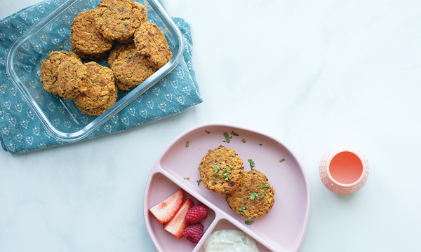 Glass dish with veggie patties on a patterned cloth; pink divided plate with patties, strawberries, raspberries, yogurt; pink cup on the side.