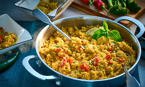 A pan of yellow rice cooked with vegetables and herbs, garnished with a lime slice and fresh basil leaves.