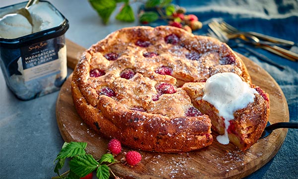Raspberry and ricotta cake dusted with icing sugar, served on a wooden board with a scoop of vanilla ice cream.