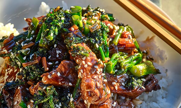 Angus beef and broccoli stir-fry served over white rice, topped with sesame seeds and spring onion.