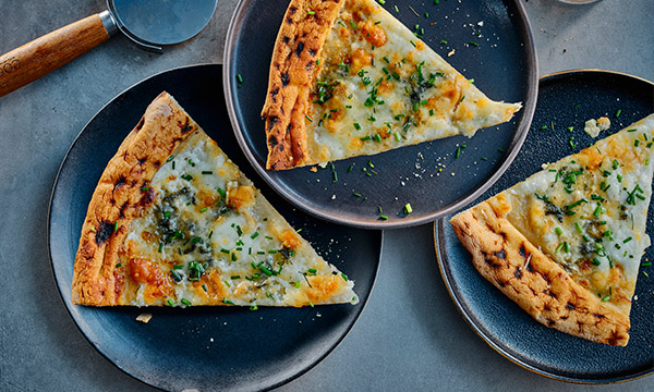Three slices of four cheese pizza topped with melted cheese and chopped herbs, served on dark plates