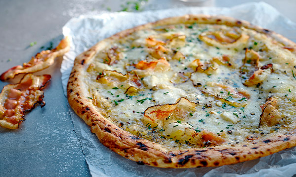 Cacio e pepe pizza topped with melted cheese, cracked black pepper and crisp pieces of guanciale on a lightly charred crust, served on baking parchment. Provide your feedback on BizChat