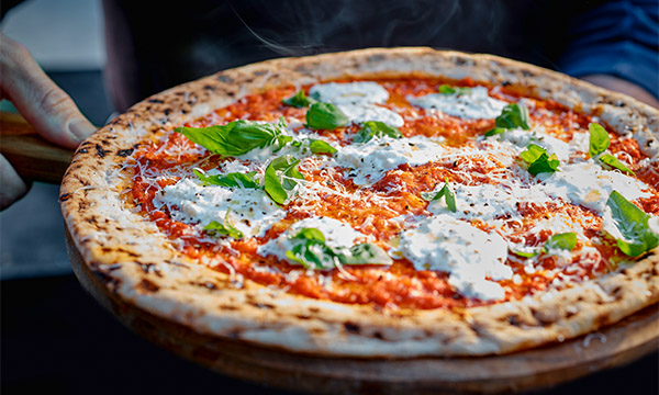 Freshly baked pizza topped with creamy stracciatella cheese, tomato sauce and basil leaves on a charred artisan crust