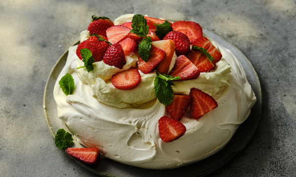 A pavlova topped with whipped cream, fresh strawberries, and mint leaves