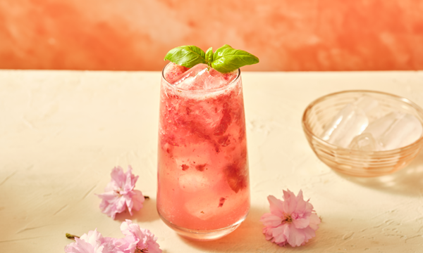 a glass filled with ice and a cocktails made with tequila, strawberries, maple syrup, basil and soda water
