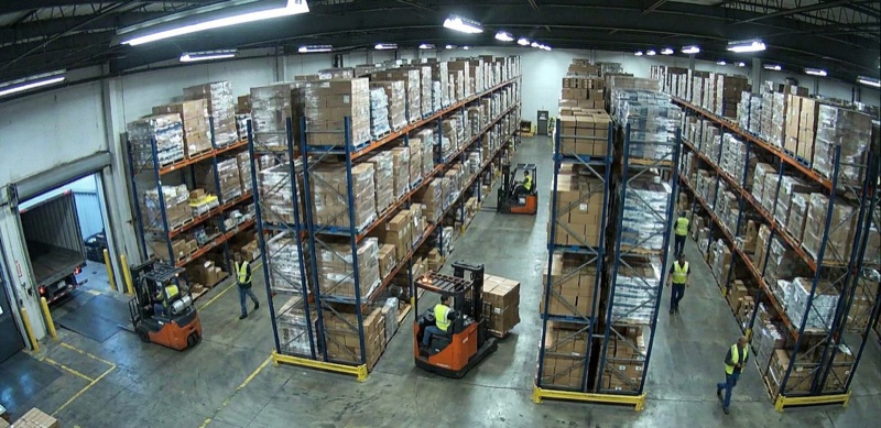 Warehouse interior with pallet racking, forklifts, and workers in high-visibility vests