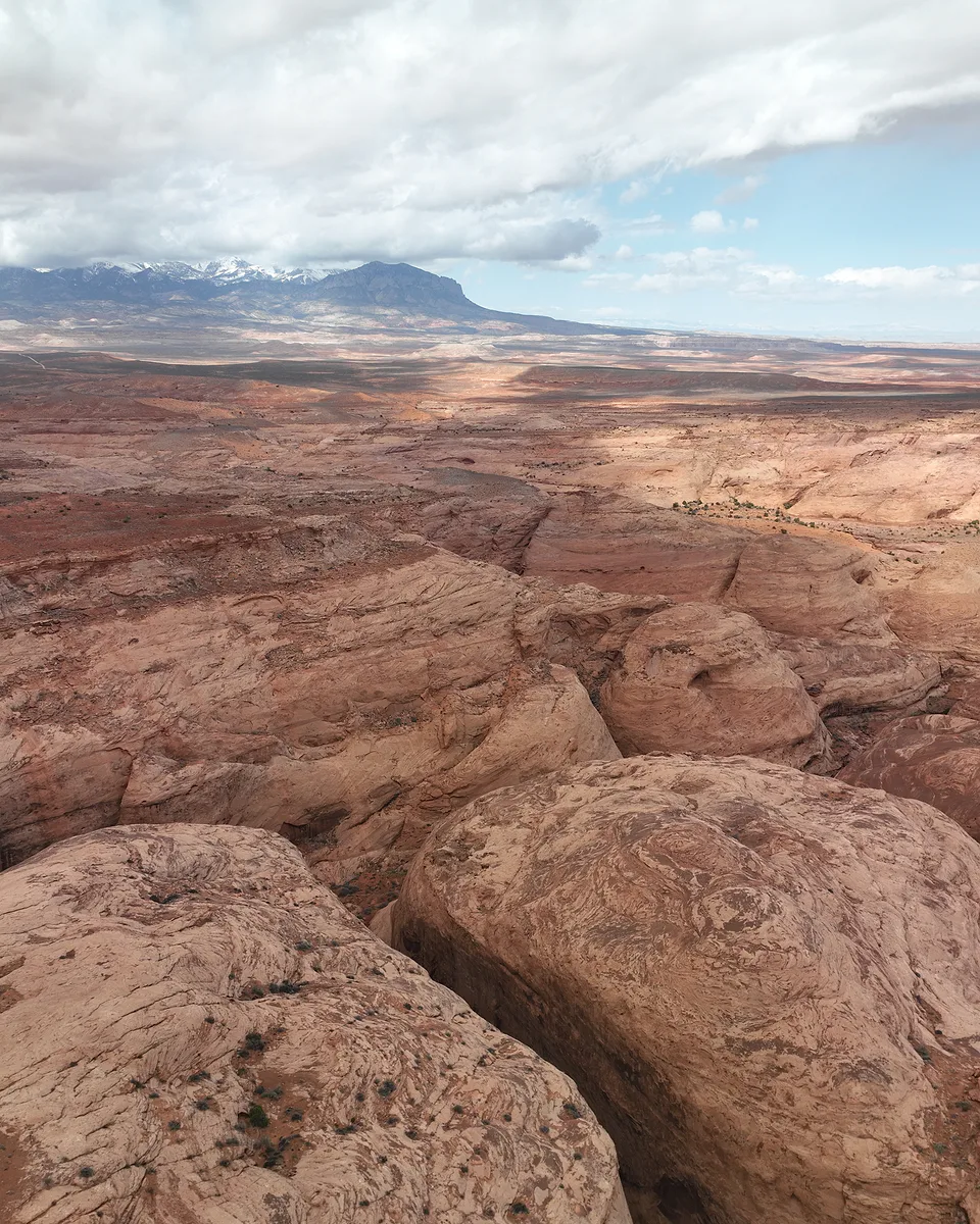 Pale slickrock canyons folding away toward a distant mesa, storm cloud over the mountains beyond