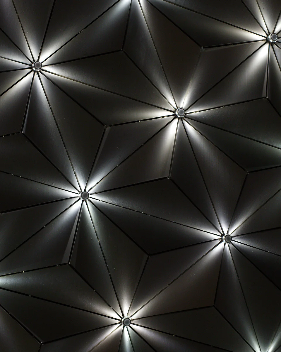 Close view of a dark geometric ceiling, starbursts of light spreading from the centre of every panel