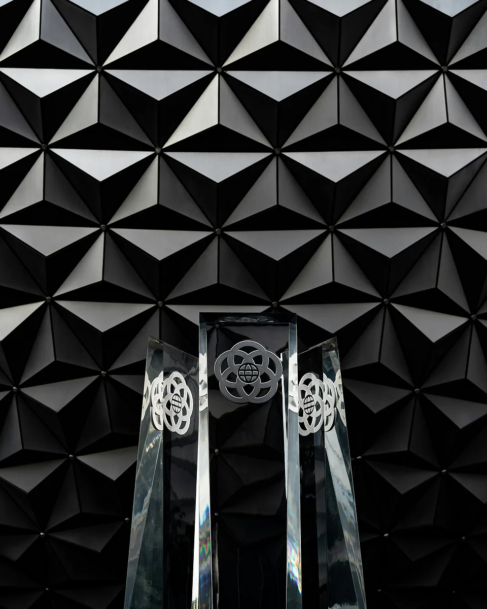Three glass awards standing before a black faceted wall of triangular panels