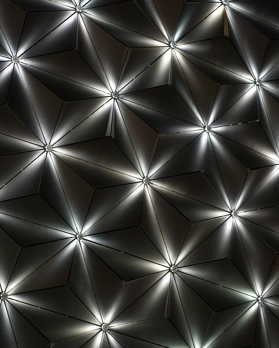 Ceiling of dark faceted panels, light radiating in spokes from a point at the centre of each triangle