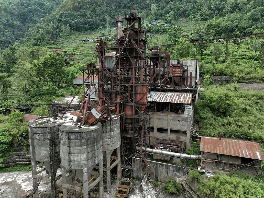 Aerial view of an abandoned industrial plant, rusted towers and concrete silos being reclaimed by green hillside