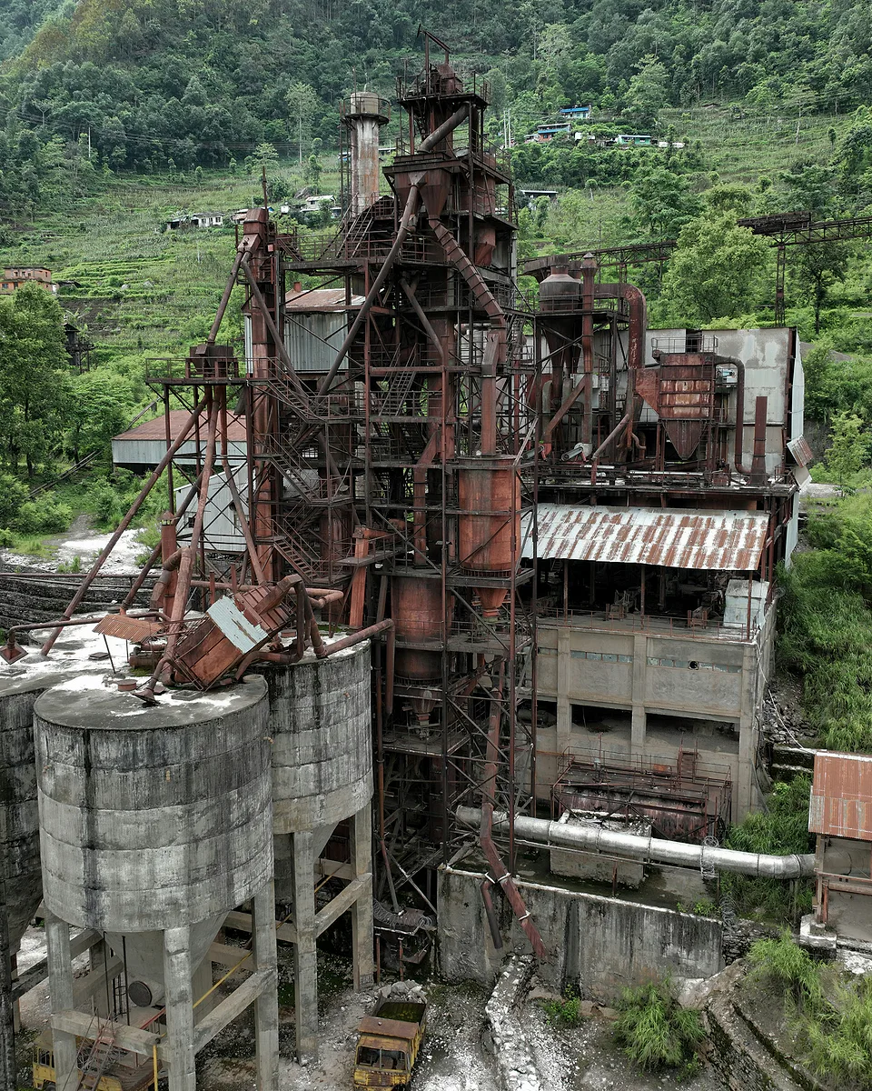 Aerial view of an abandoned industrial plant, rusted towers and concrete silos being reclaimed by green hillside