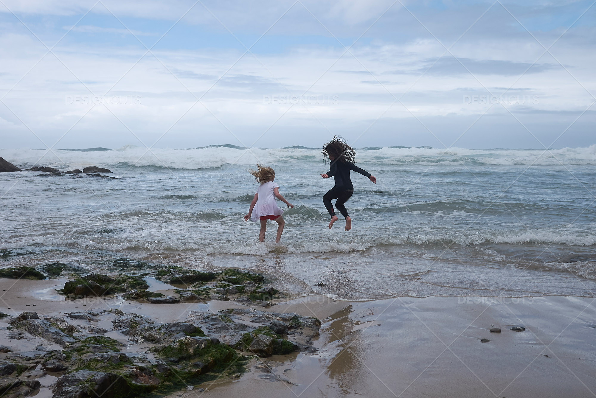 Two Children Play On Shore Of Stormy Beach