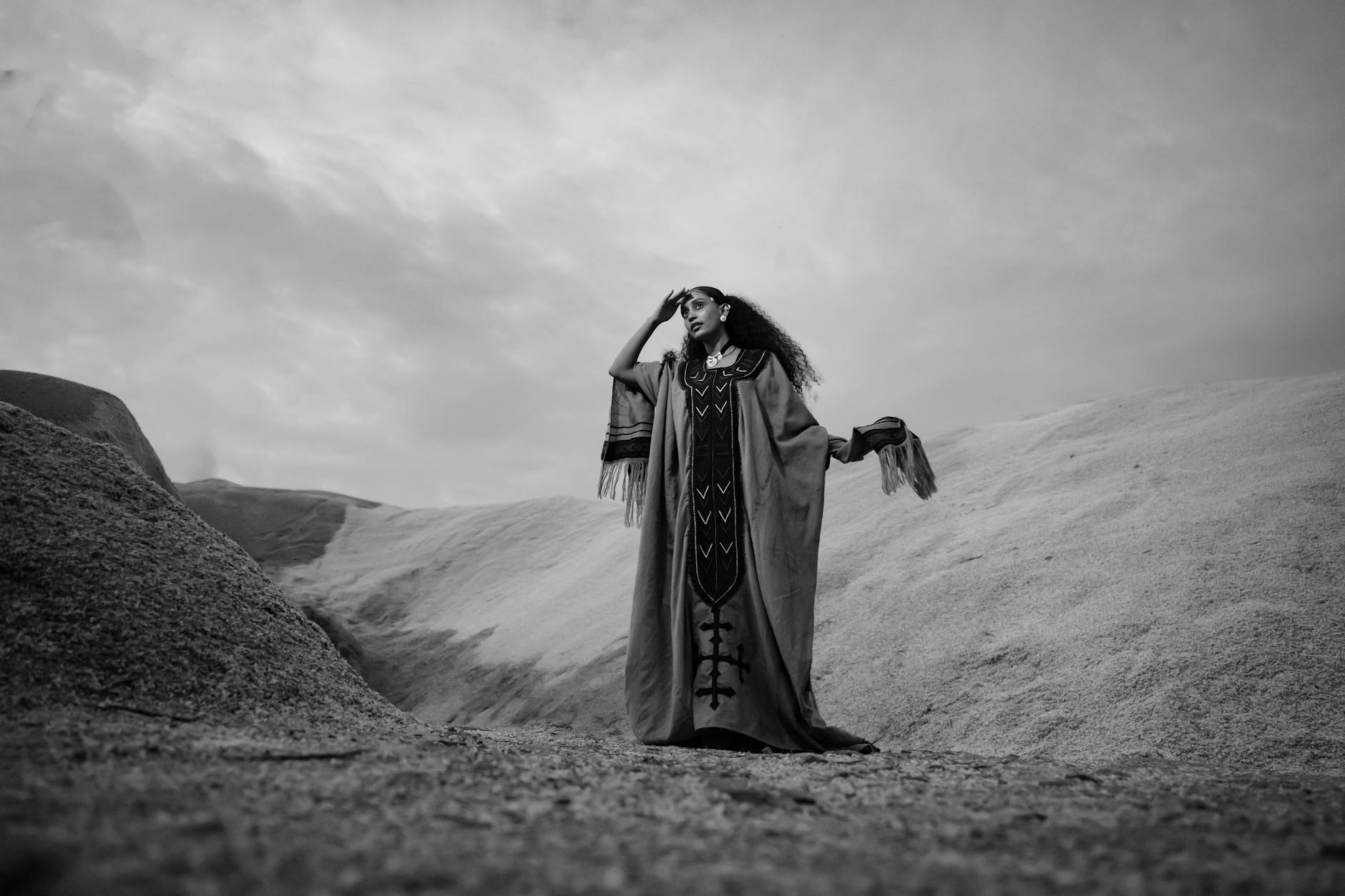 Black and white photo of a woman in traditional Ethiopian dress standing in a desert landscape.