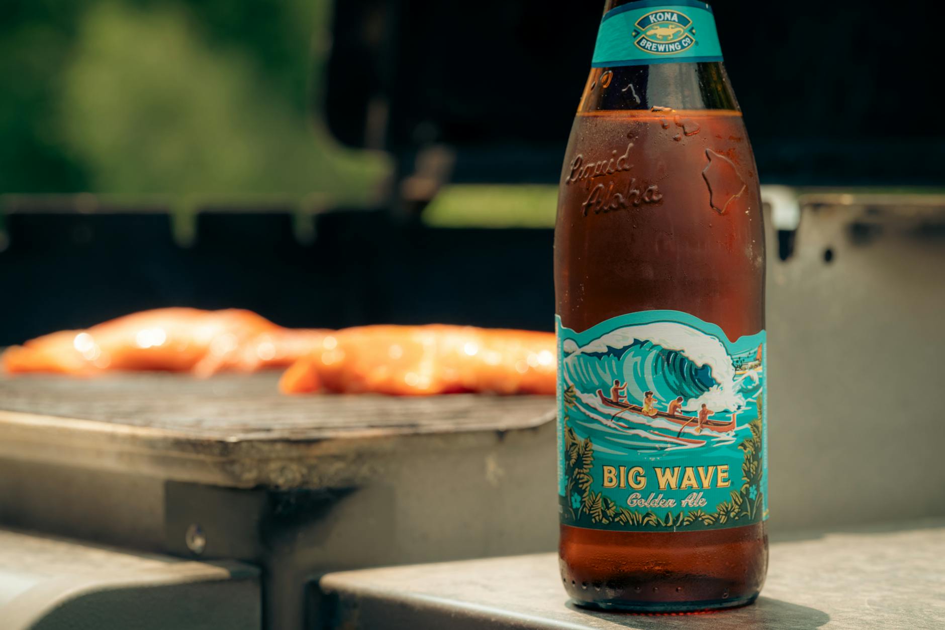Craft beer bottle with wave label and grilled food in sunny outdoor setting.